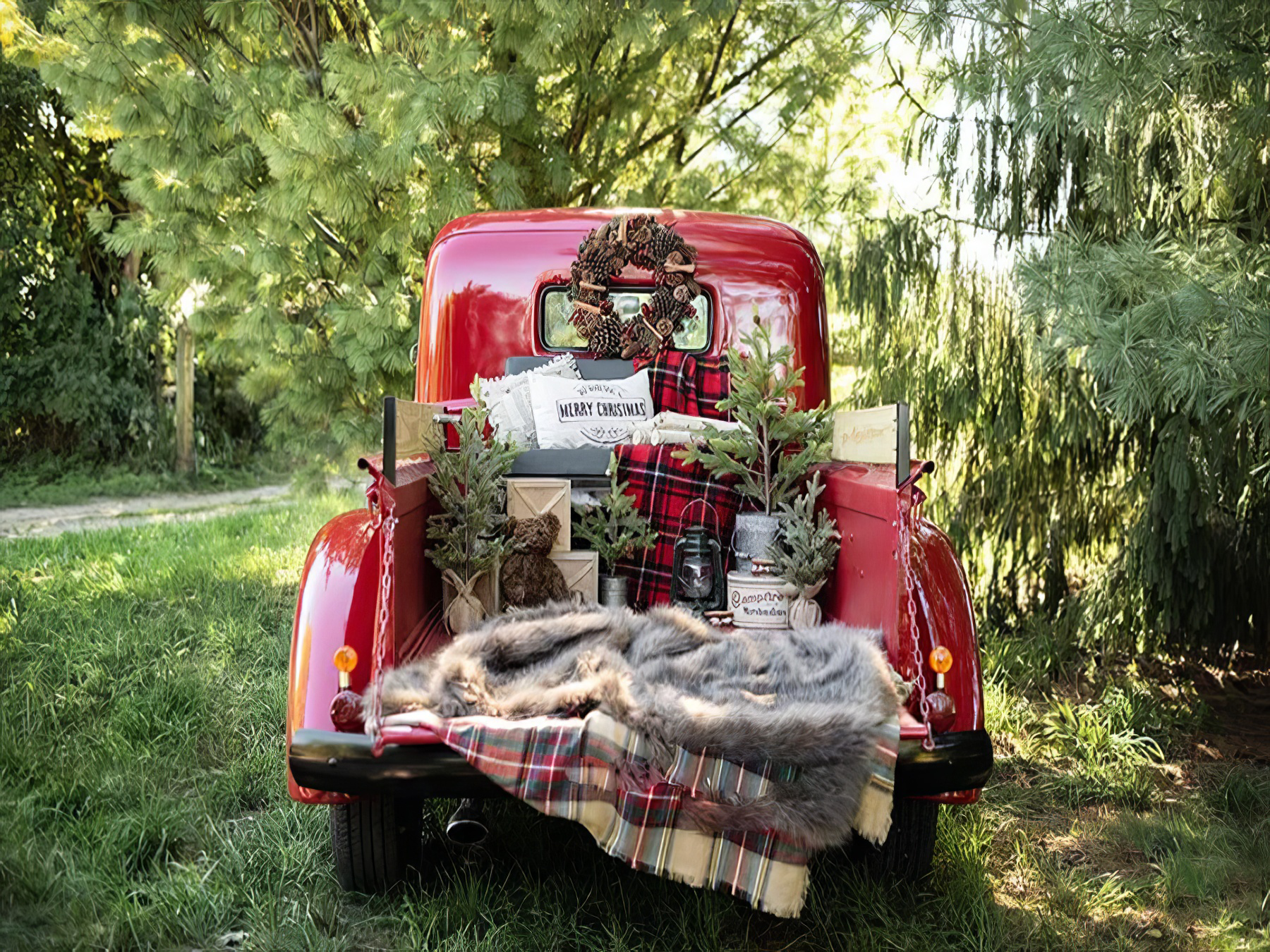 Vintage red truck decorated for Christmas with wreath, plaid blankets, gifts, and mini trees in the truck bed.