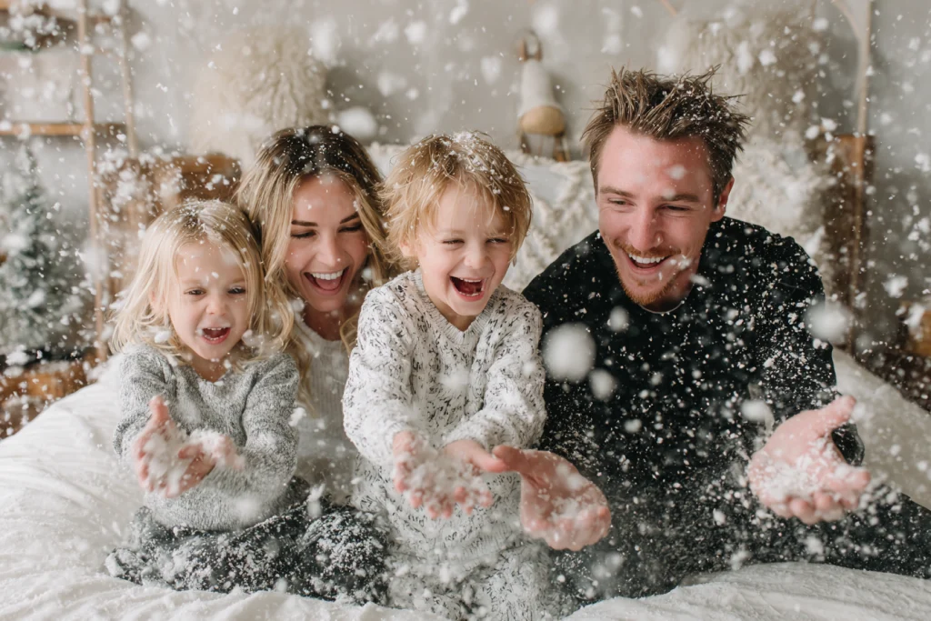 Family laughing together while tossing faux snow in a Christmas studio setup.