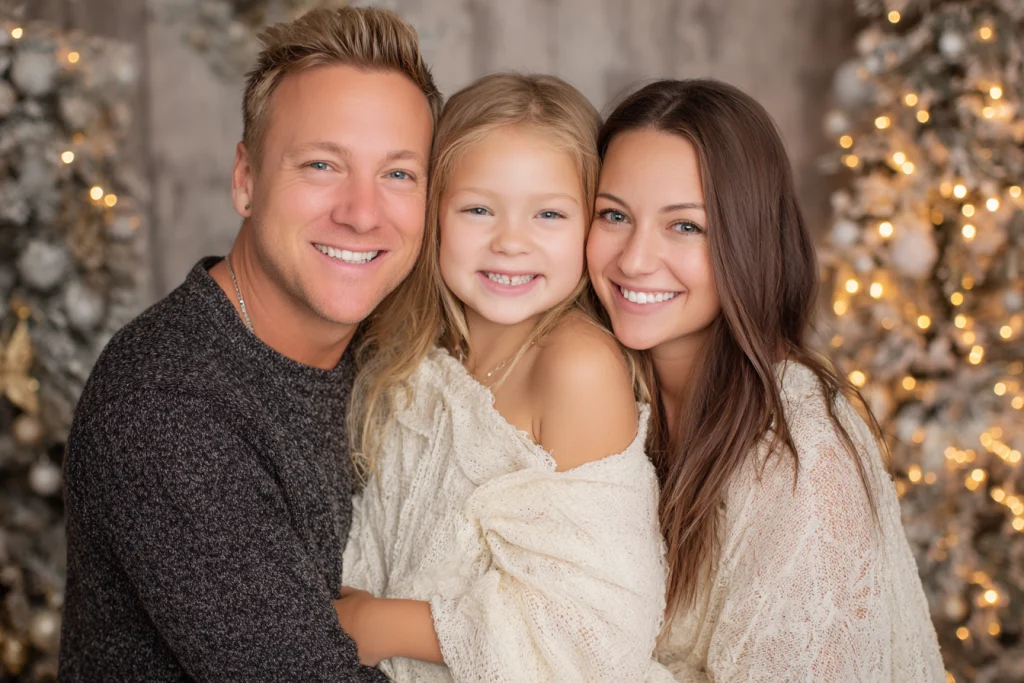 Family hugging in front of a glowing Christmas tree during holiday portraits.