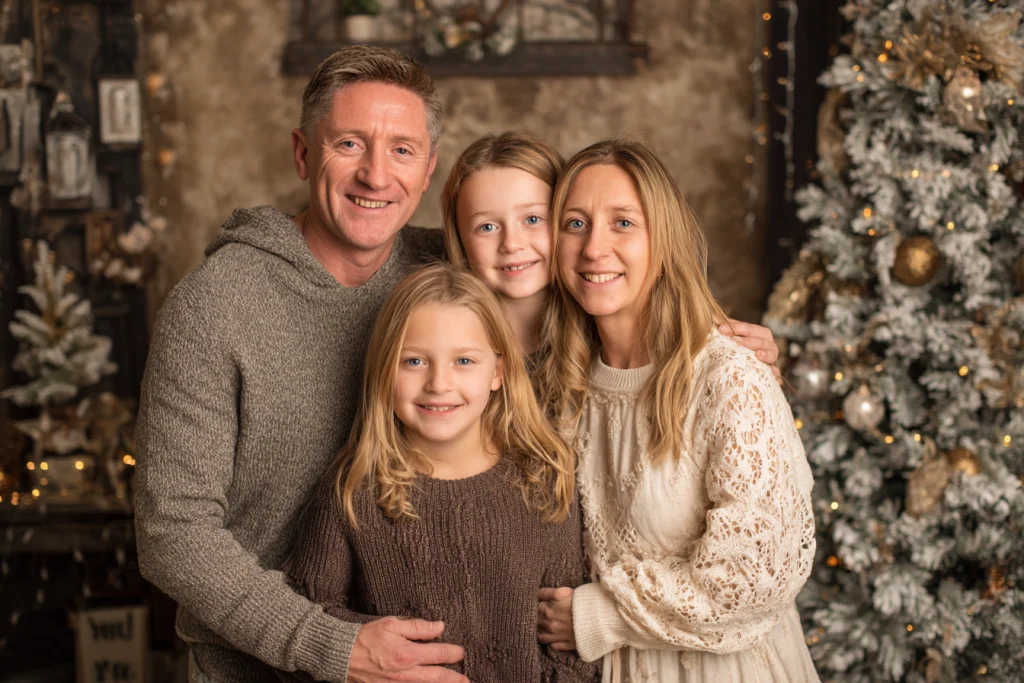 Family hugging in front of a glowing Christmas tree during holiday portraits.