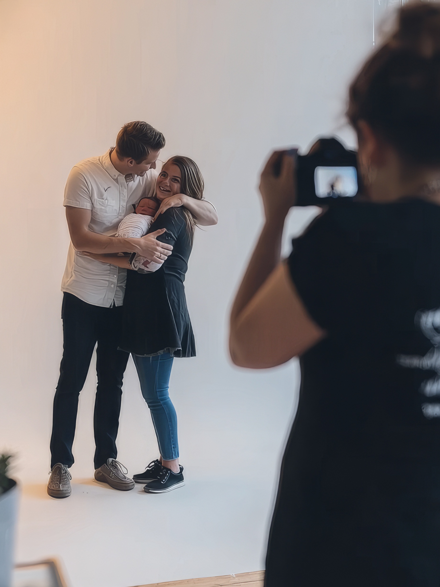 Female photographer taking photo of a young couple holding their newborn in a studio setup