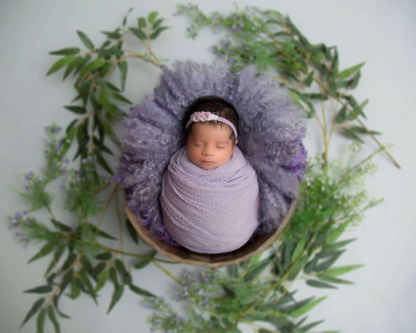  A picture of a baby sleeping inside a basket with greenery around them
