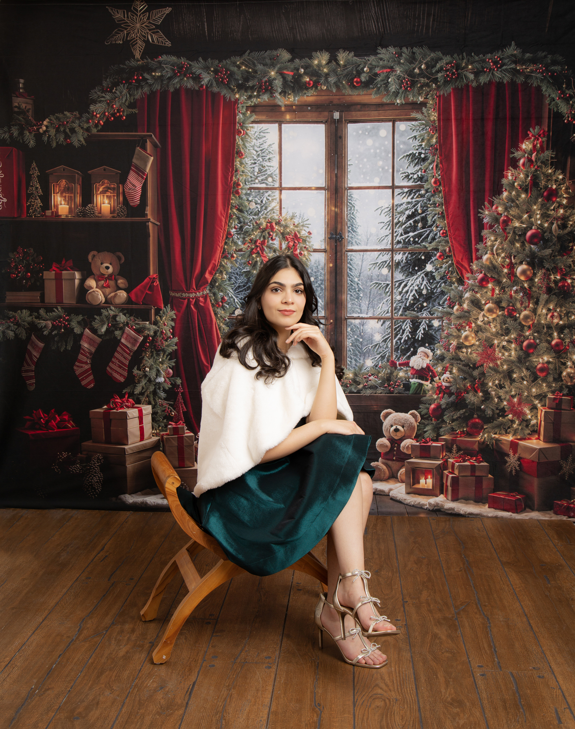 Woman in a green dress and white shawl posing in a Christmas studio with decorated tree, red curtains, and wrapped presents.